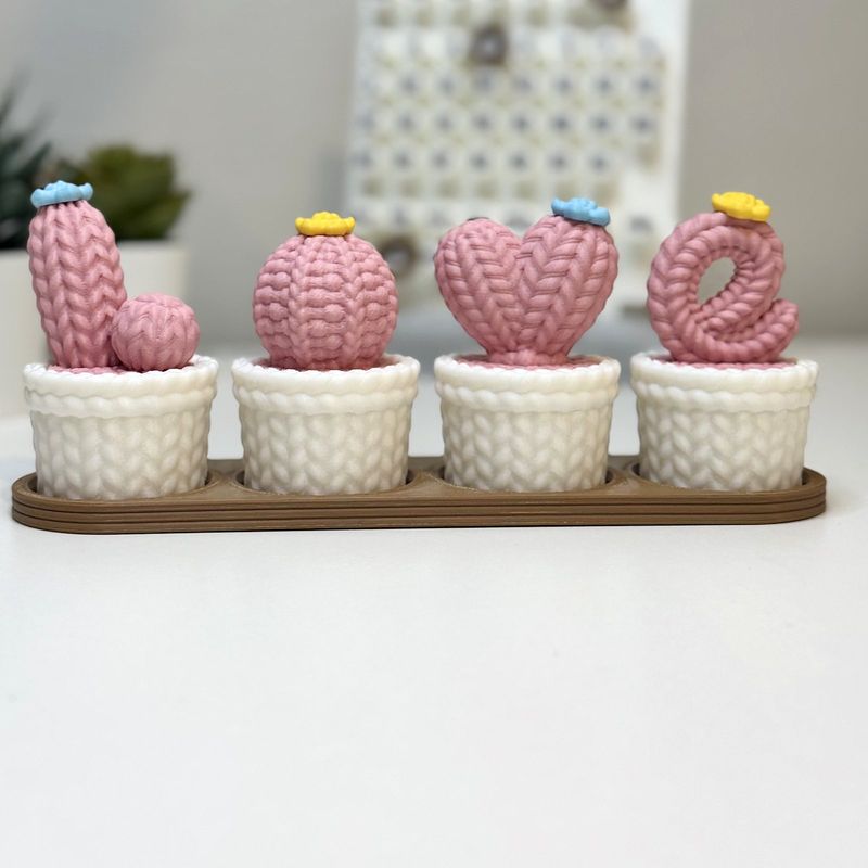 Four pink cacti in white pots spelling LOVE on a brown tray